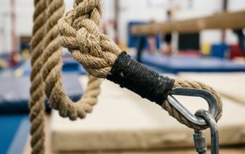 Gymnast climbing a thick natural fiber rope inside a bright athletic facility.